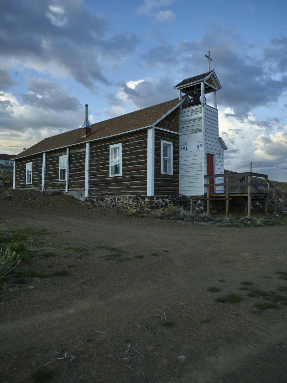 A white clapboard one-room schoolhouse with a green roof and a small bell tower standing on bare ground at Atlantic City, Wyoming, under a cloudy sky.
