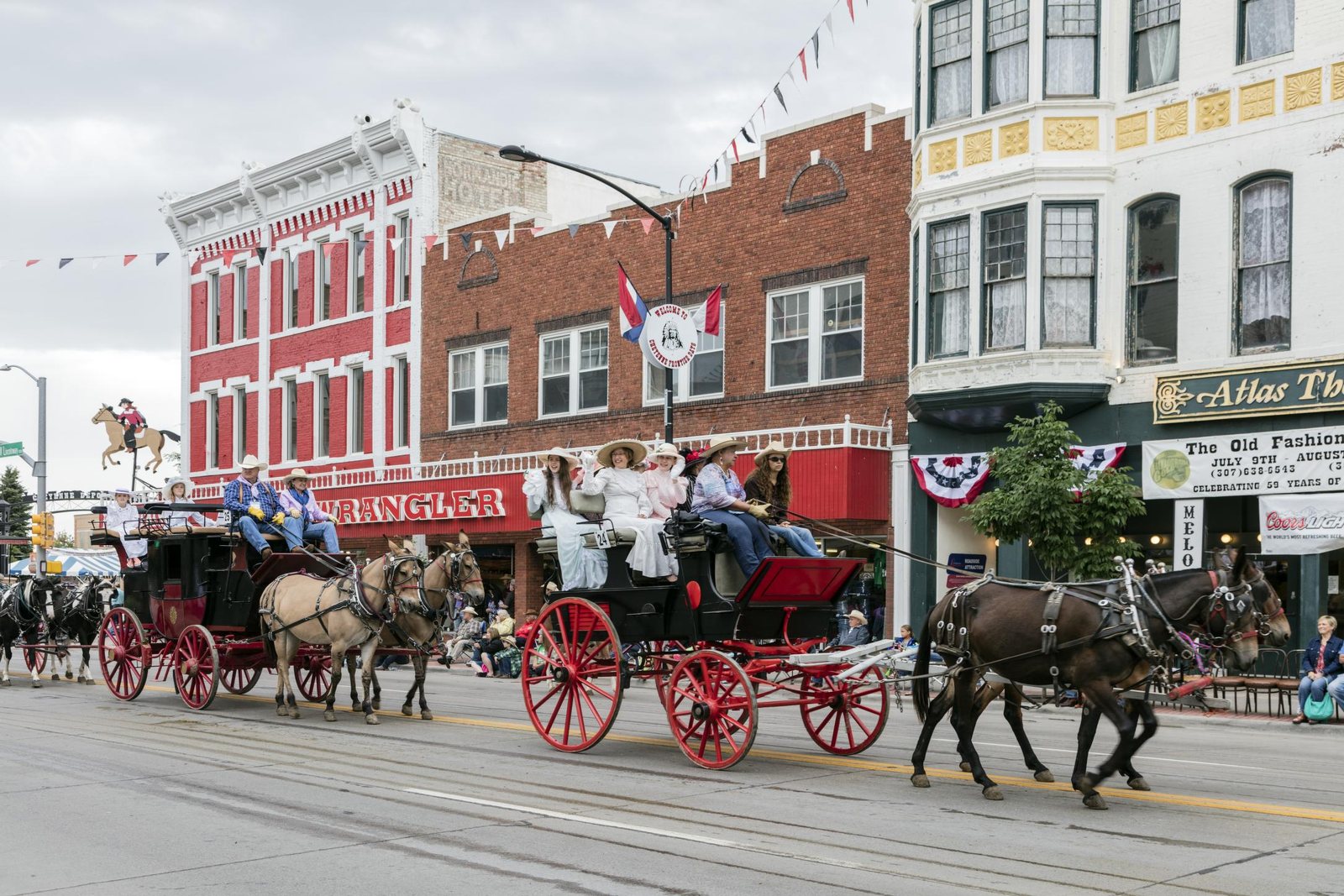 A horse-drawn stagecoach with a four-up hitch rolling down a bunting-hung street in downtown Cheyenne past red brick storefronts, spectators watching from the kerb.