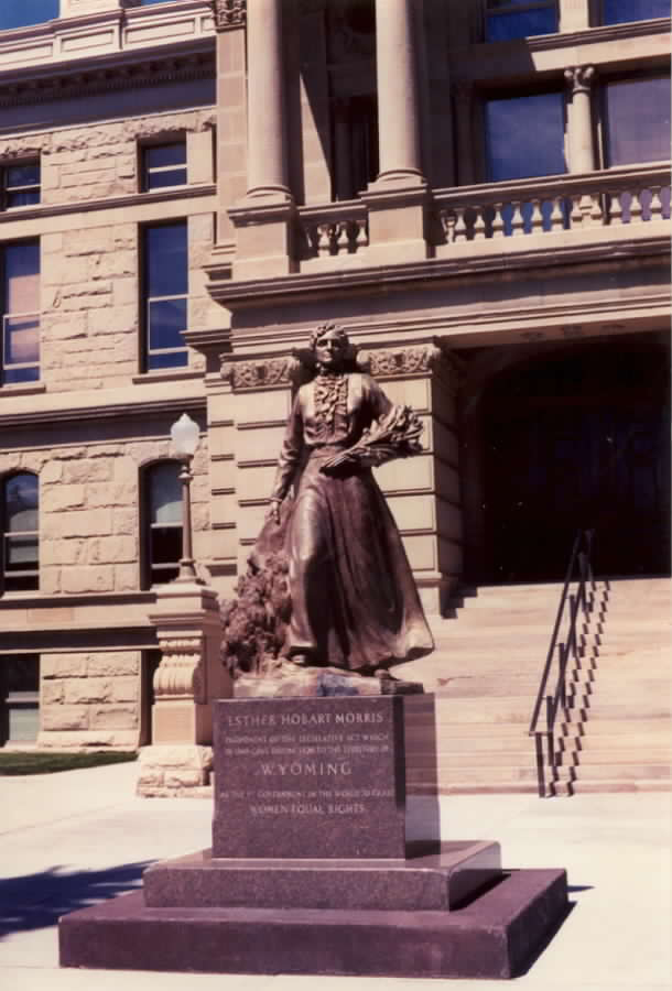 Statue of Esther Hobart Morris in front of the Wyoming State Capitol in Cheyenne, in heavy bronze with raised hand.