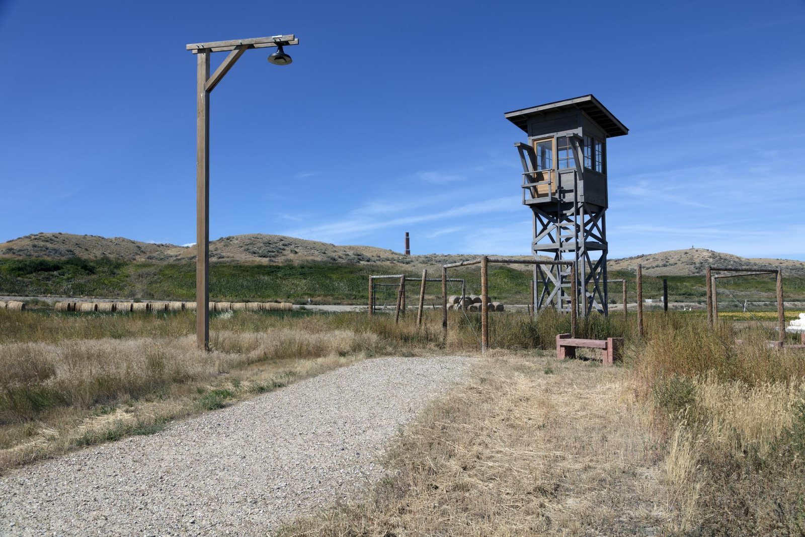 A wooden guard tower standing beside a gravel path in dry open grassland at the former Heart Mountain Relocation Center, Park County, Wyoming, under a clear sky.