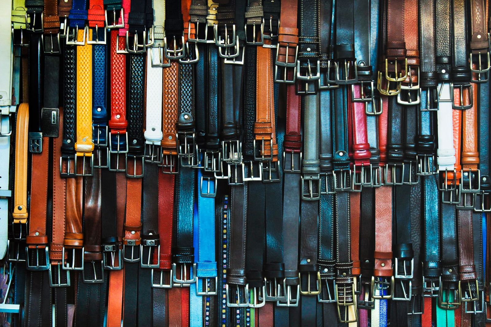 Rows of leather belts in many colors hanging side by side in a shop, buckles at the top.