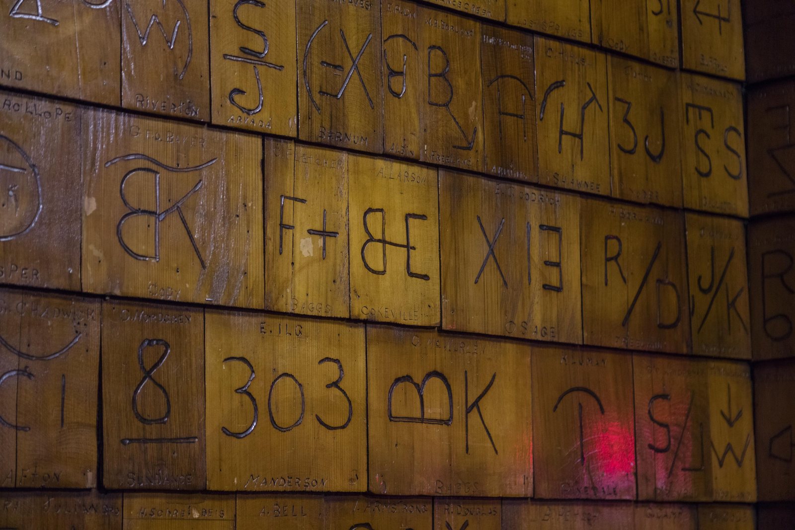 Cattle brands burned into the varnished wooden wall of the Mint Bar in Sheridan, Wyoming, dozens of them in rows, including a numeral brand reading 303.