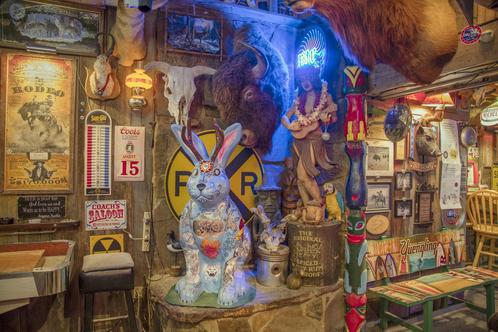 The crowded interior of the White Wolf Saloon in Douglas, Wyoming, with a life-size painted jackalope, a mounted bison head, vintage tin signs, a jukebox, and an old advertising thermometer on the wall.