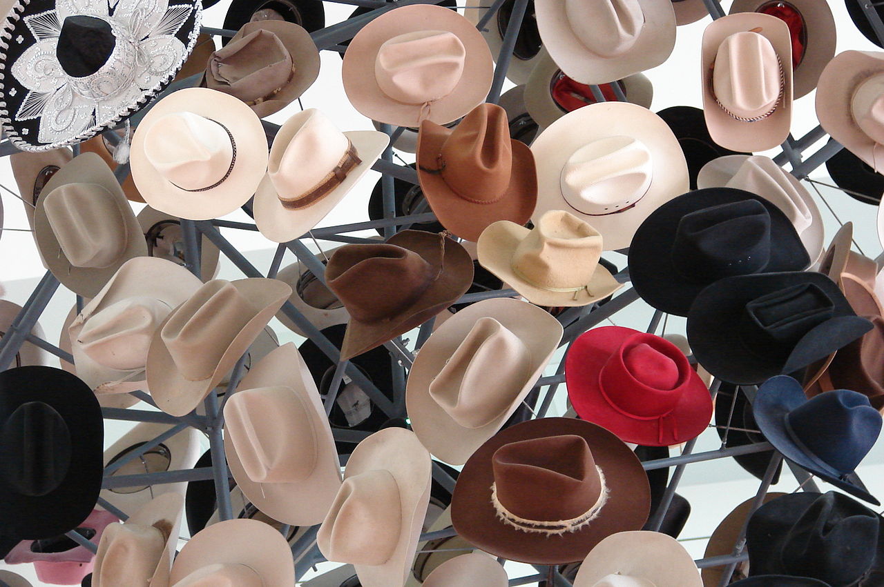 A display of cowboy hats in a Fort Worth, Texas Western wear store: multiple felt and straw styles in natural tan, brown, and off-white, stacked and arranged on a rack with varying crown heights and brim widths.