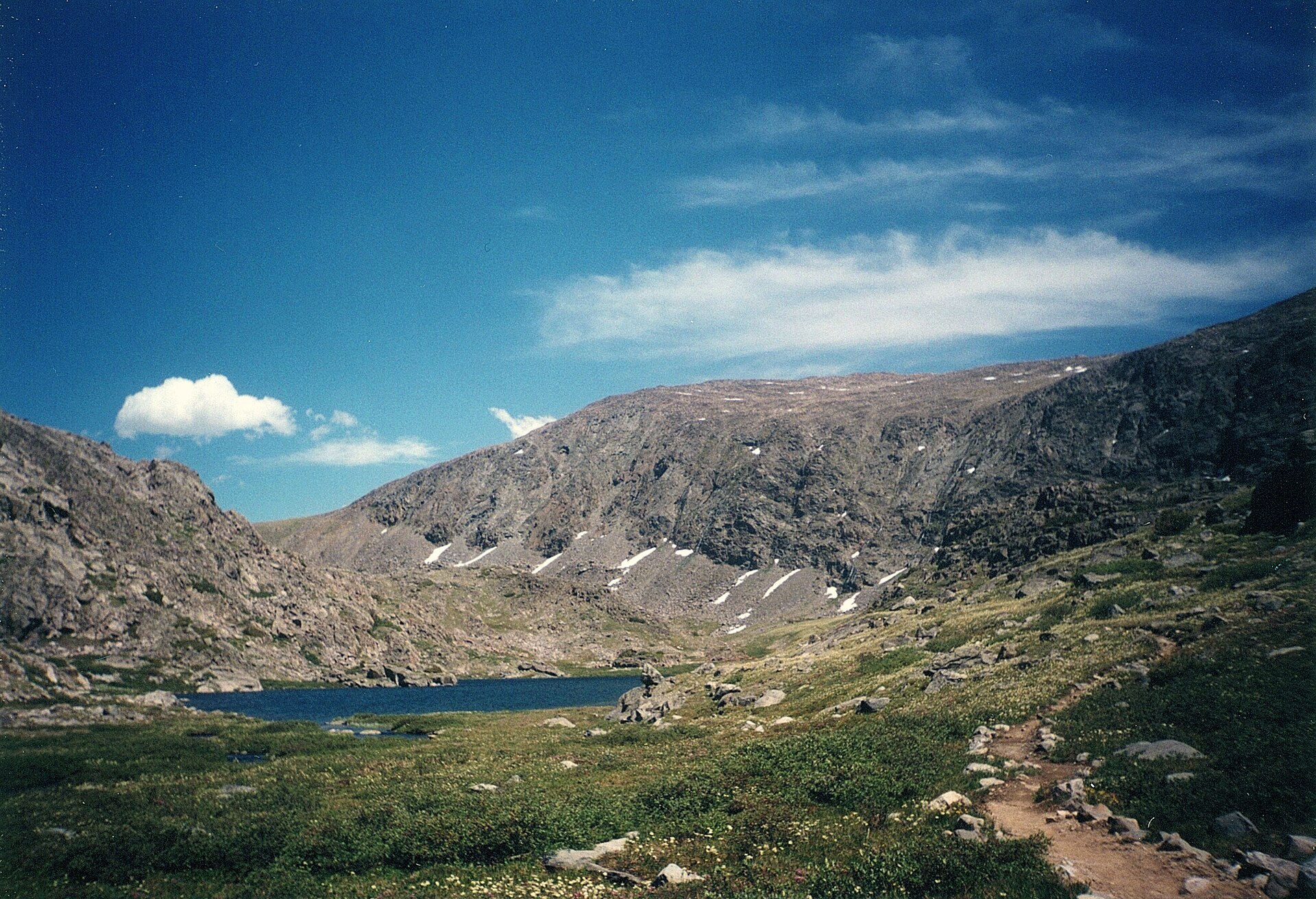 High-altitude tundra in the Wyoming Bighorn Mountains, with low alpine vegetation, scattered rock outcrops, and a distant ridgeline under a wide sky — the terrain where a properly-made bedroll earns its keep.