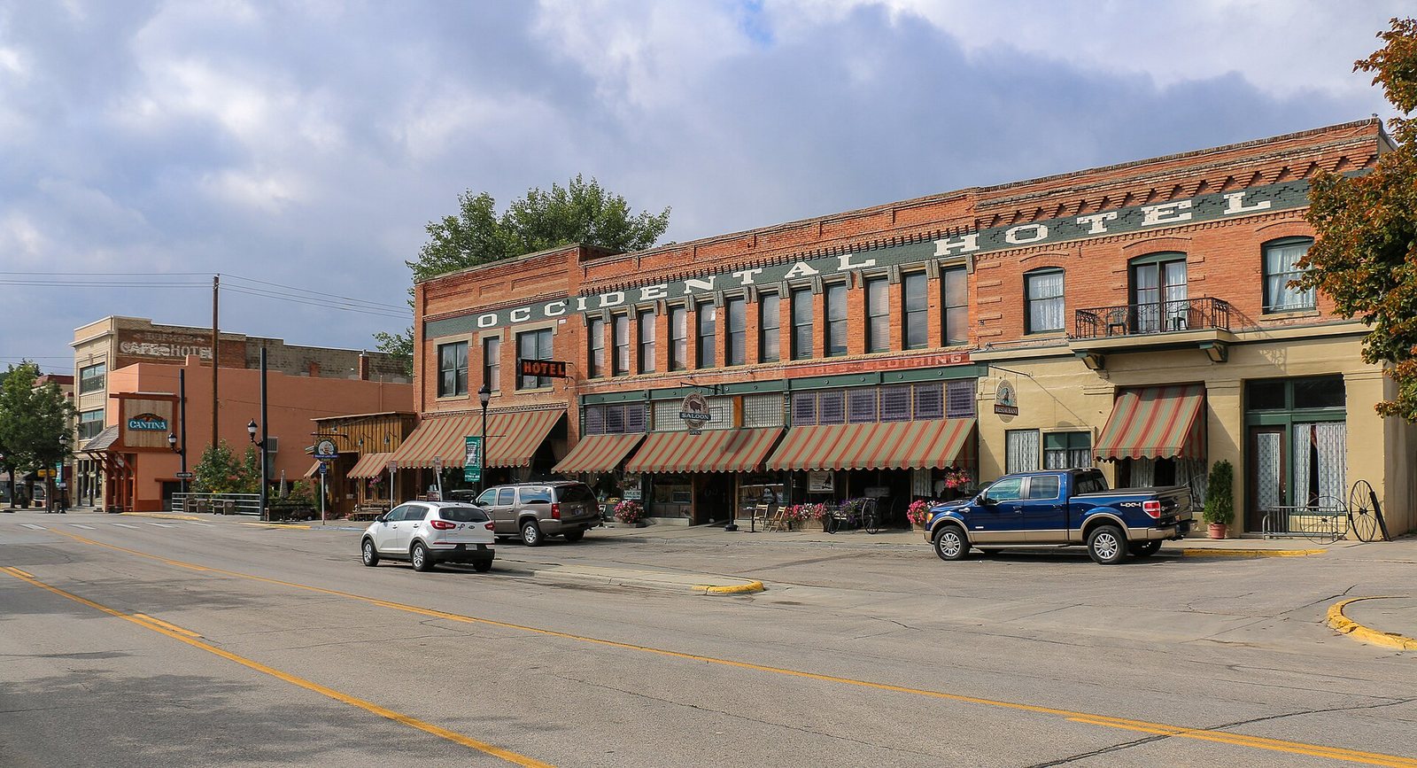 The Occidental Hotel in Buffalo, Wyoming, a long two-storey red brick building with a row of shopfront awnings along a wide, quiet main street under a partly clouded sky.